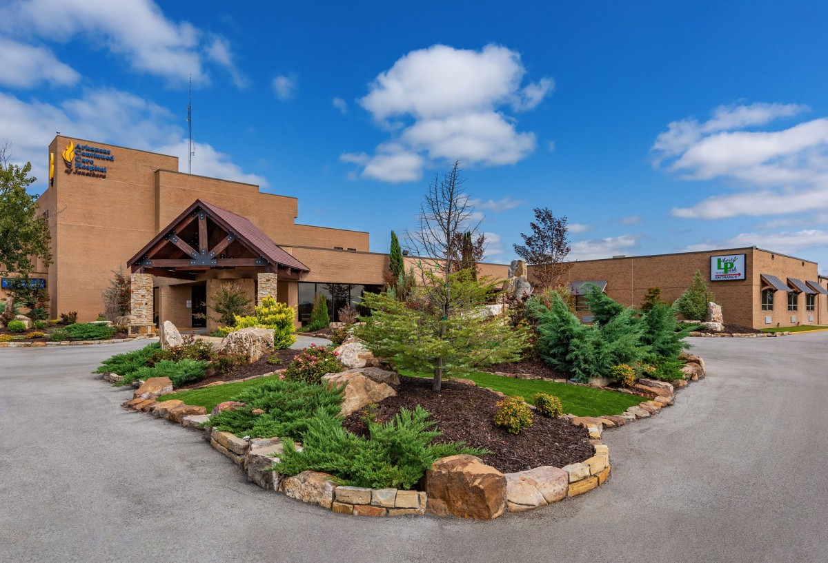 A beautifully landscaped entrance to a building with clear blue skies and scattered clouds.