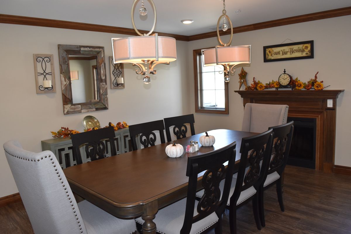 A well-decorated dining room featuring a large table with chairs and elegant chandeliers, complemented by a mirror and seasonal decorations.