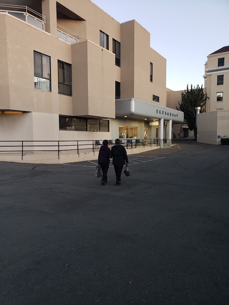 Two people walking towards a hospital building in the evening.