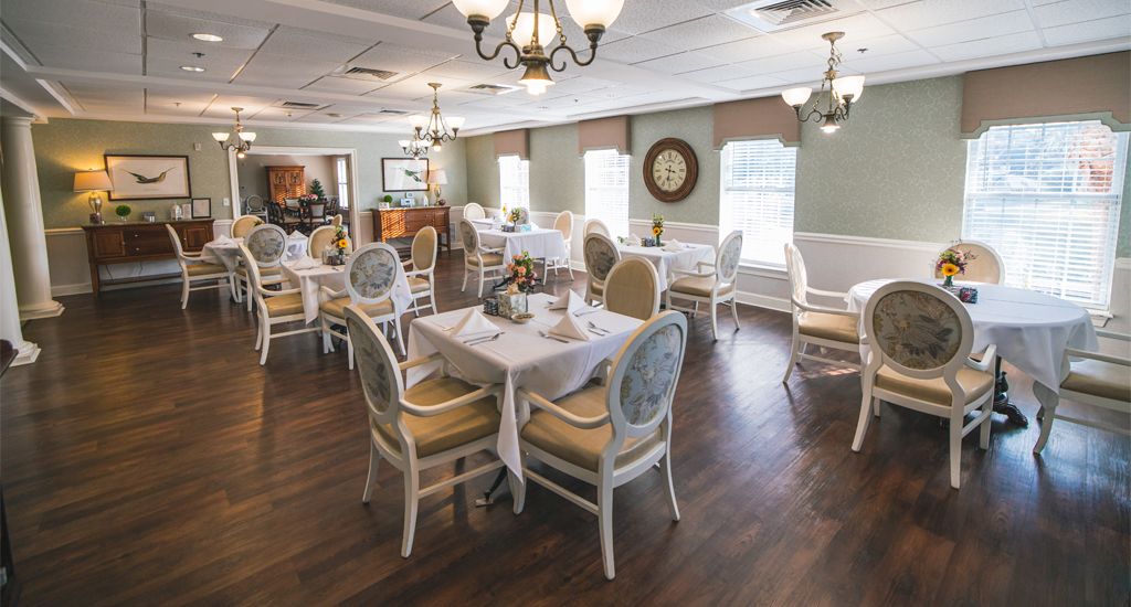 An elegant restaurant dining room with neatly arranged tables and chairs, decorated with chandeliers.