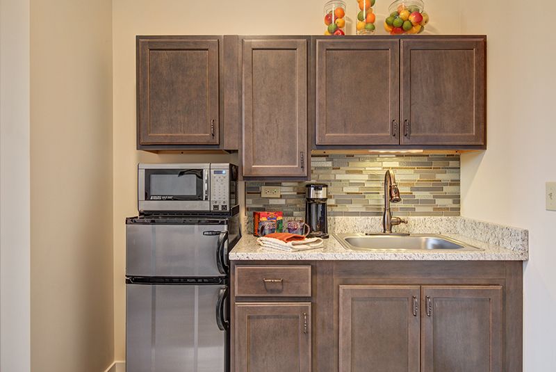 A compact kitchen setup featuring wooden cabinets, a microwave, a small fridge, and a sink with a modern backsplash.