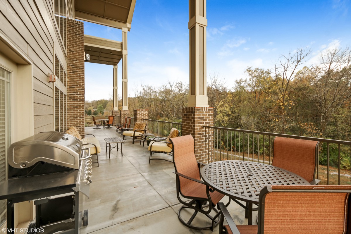 A spacious outdoor patio with seating and barbecue grills overlooking a wooded area.
