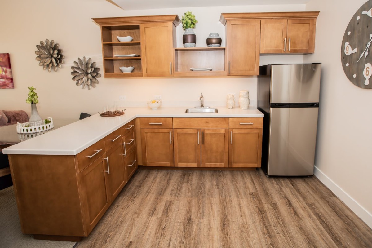 A modern kitchen with wooden cabinets, a stainless steel refrigerator, and wood flooring.