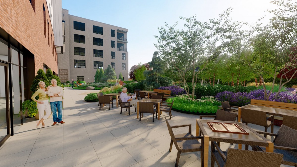 A peaceful outdoor patio area with wooden furniture, surrounded by lush greenery and a building in the background.