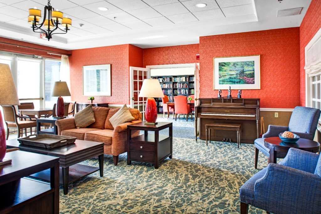 A cozy living room with a piano and bookshelves, featuring warm decor and comfortable seating.