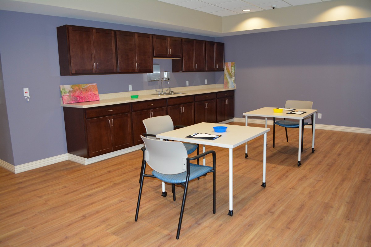 A tidy room with tables, chairs, and a kitchen area featuring wooden cabinets.