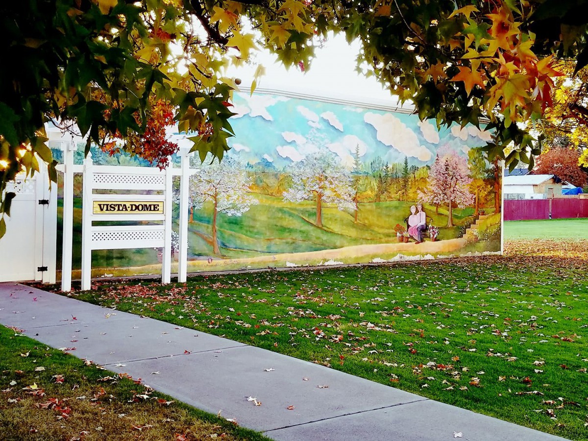 A scenic mural depicting a landscape is framed by autumn trees and a sidewalk.