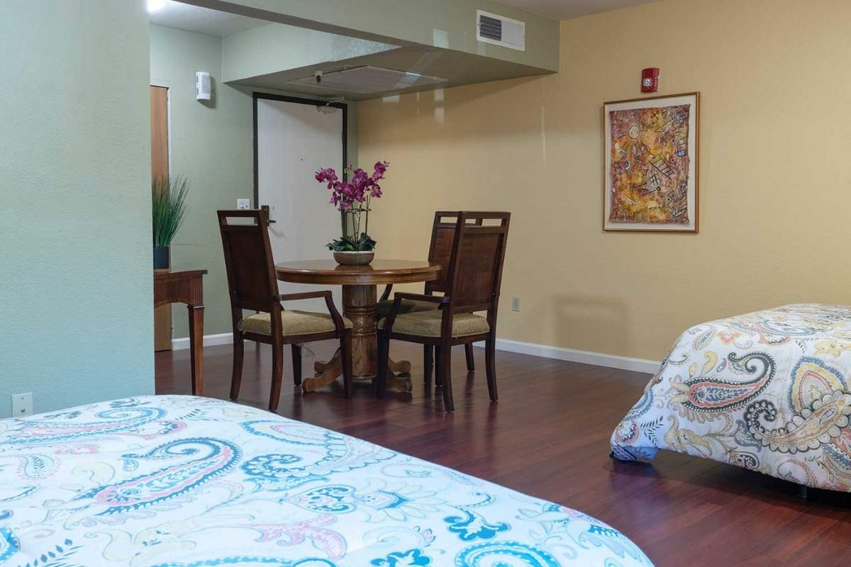 A cozy dining area with a round table and chairs, adorned with flowers, adjacent to a bed in a warmly decorated room.