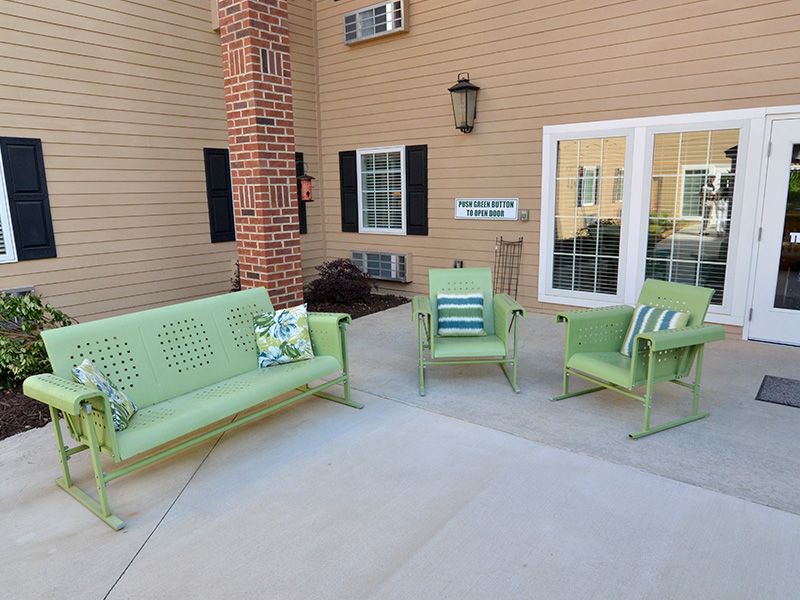 An outdoor patio area with green metal seating, including a sofa and chairs, adorned with colorful striped pillows against a brick wall backdrop.