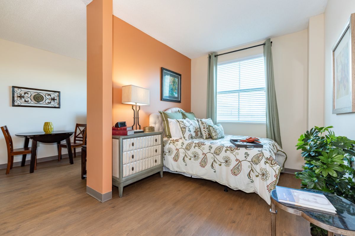 A cozy bedroom with a floral bedspread, side table with a lamp, and a large window.