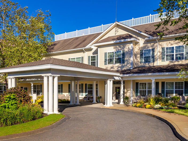 A sunny view of a large residential building with a driveway and entrance.