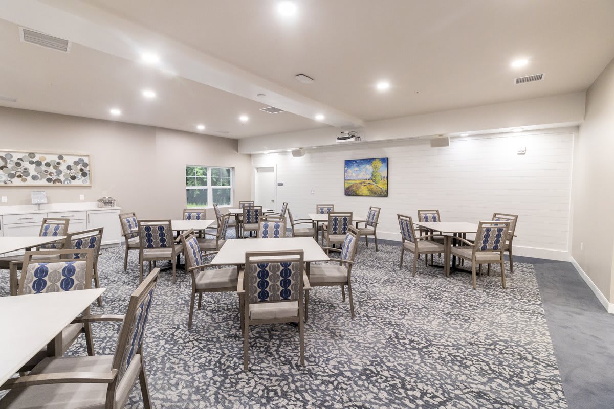 A well-lit dining area with neatly arranged tables and upholstered chairs on a patterned carpet.