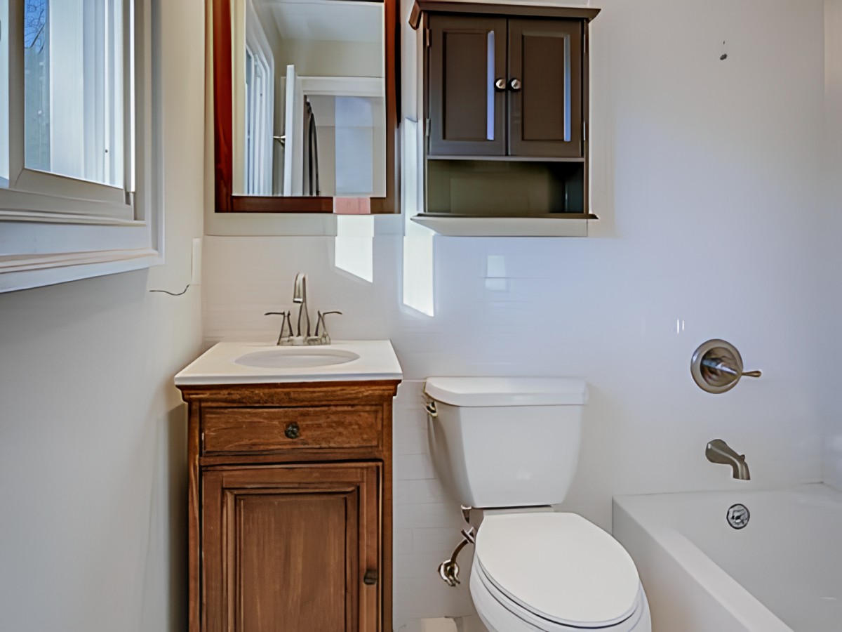 A compact bathroom with a wooden vanity, white toilet, and a bathtub.