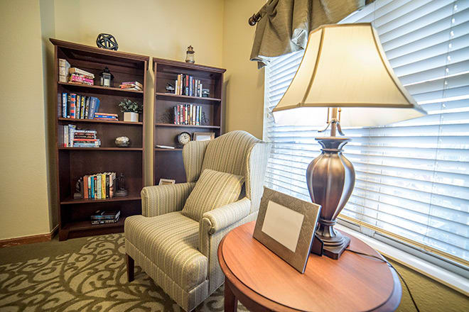 A cozy reading corner with an armchair, bookshelf, and a lamp by the window.