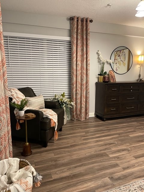 Cozy living room with an armchair, decorative plants, and a dresser under a round mirror.
