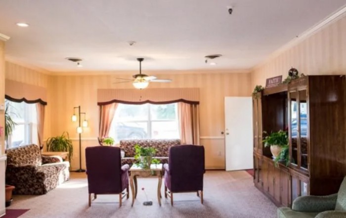 A cozy living room with armchairs and a window, decorated with plants and a ceiling fan.