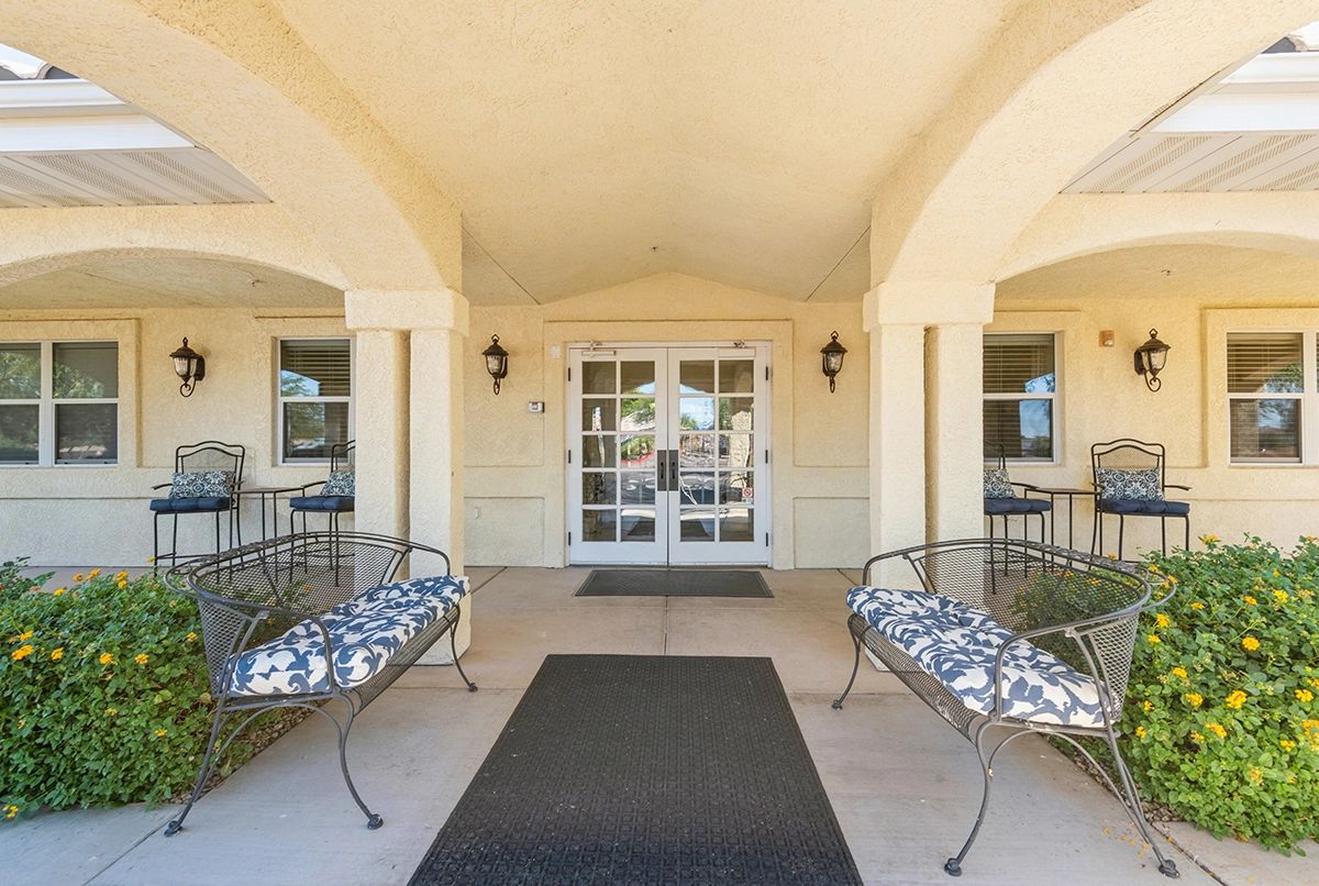 The covered entrance of a building with benches on either side and glass double doors.