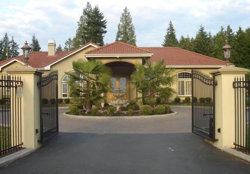 A gated residential house with a circular driveway and landscaped front yard.