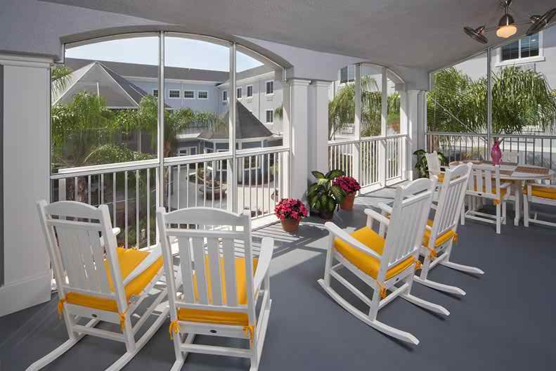 A sunny porch area with yellow-cushioned rocking chairs and potted plants.