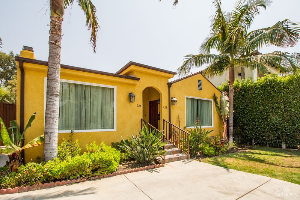 A vibrant yellow house with surrounding palm trees and lush landscaping.
