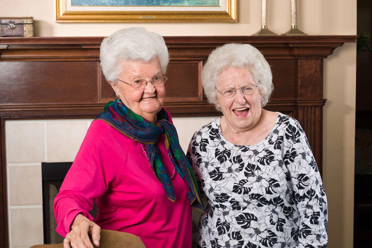 Two elderly women smiling and enjoying each other's company indoors.