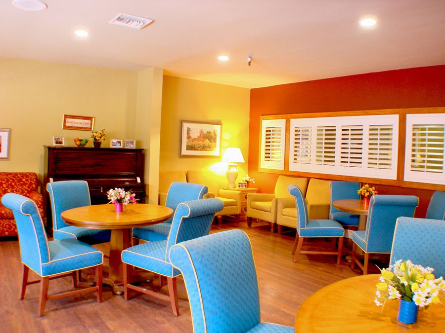 A cozy dining area with blue chairs, wooden tables, and a piano in the corner.