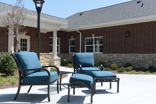 A set of blue cushioned outdoor chairs arranged on a sunny patio, surrounded by well-maintained landscaping.