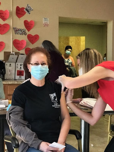 A woman receiving a vaccine while wearing a mask in a community healthcare setting.