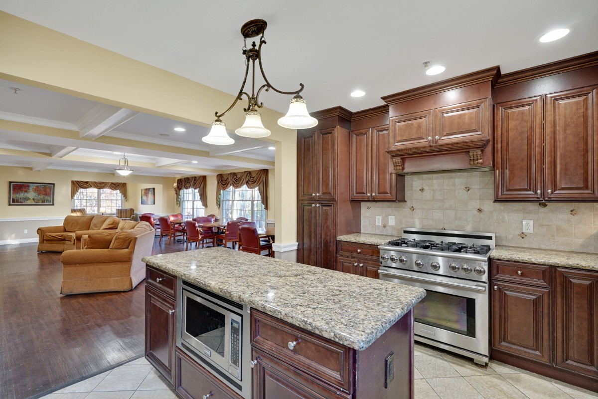 A modern kitchen featuring a central island with granite countertops, wood cabinetry, and a stainless steel stove.