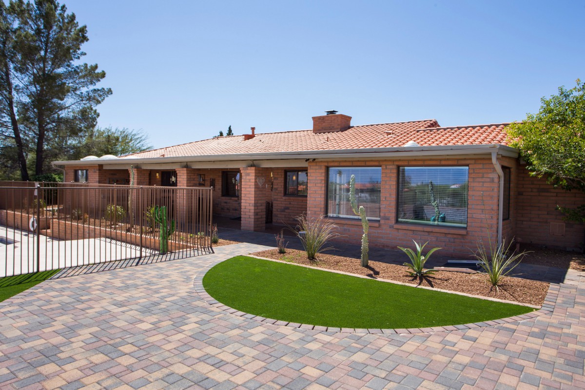 A single-story brick house with a tiled roof, featuring a landscaped yard and paver walkway.