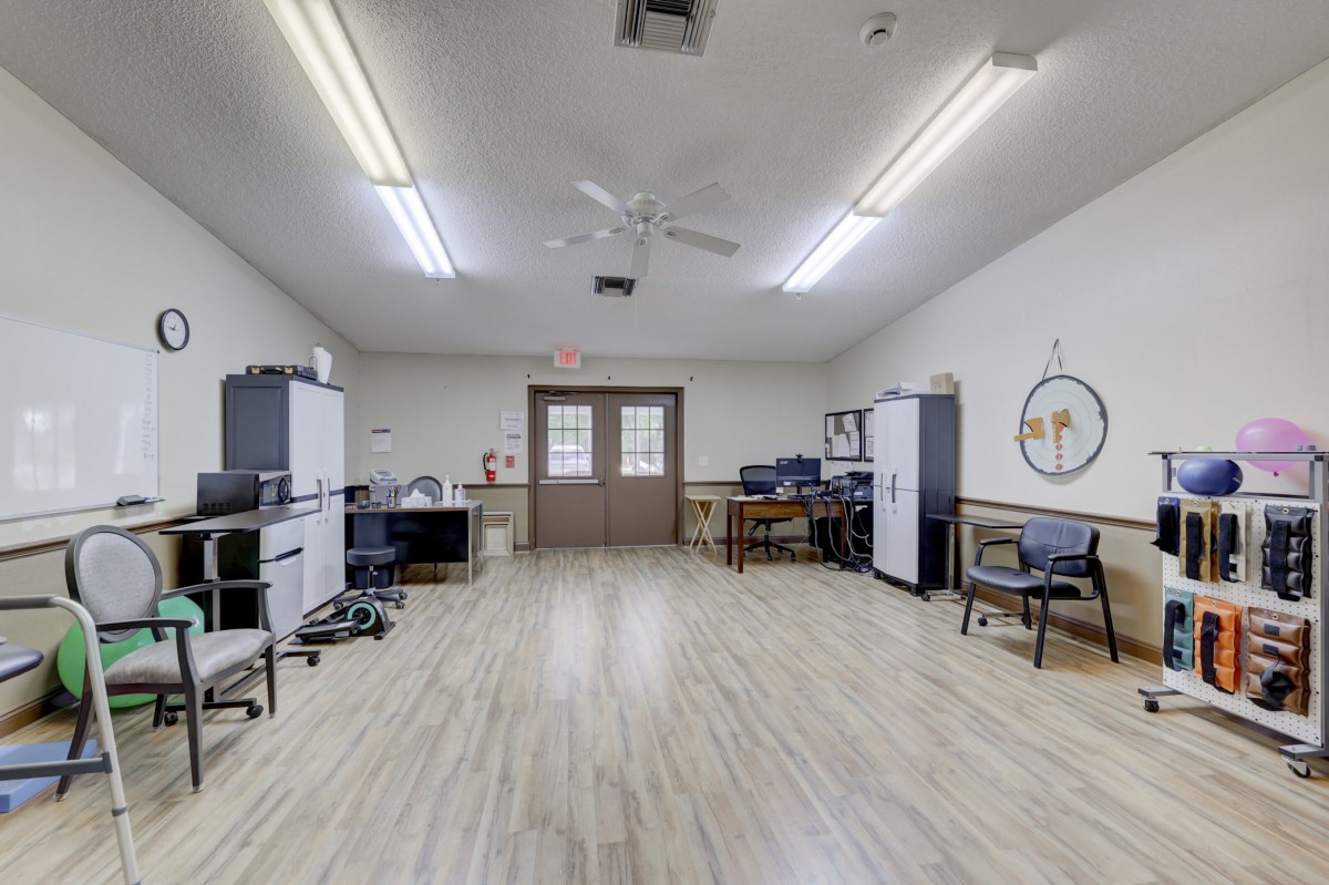 An empty office space with desks, chairs, and computers under florescent lighting.