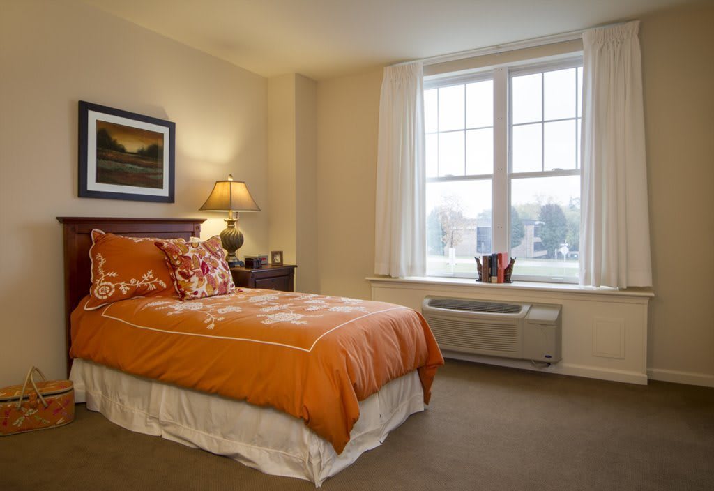 Cozy bedroom with orange bedding and a large window.