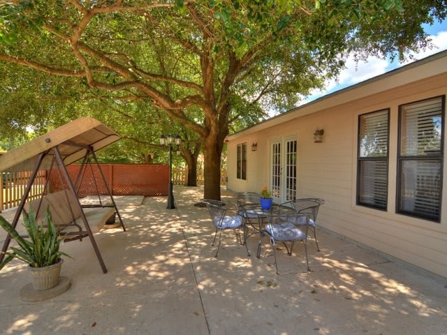 A tranquil backyard patio with outdoor seating under the shade of large trees.