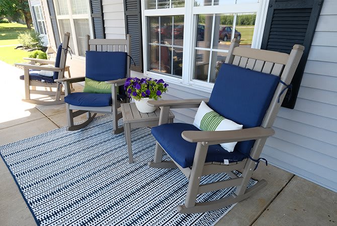 A cozy porch setup with two rocking chairs, blue cushions, and a pot of flowers.