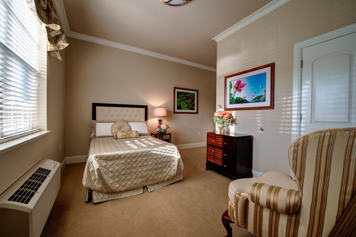 A cozy and elegant bedroom interior with a bed, nightstand, lamp, artwork, and a striped chair.