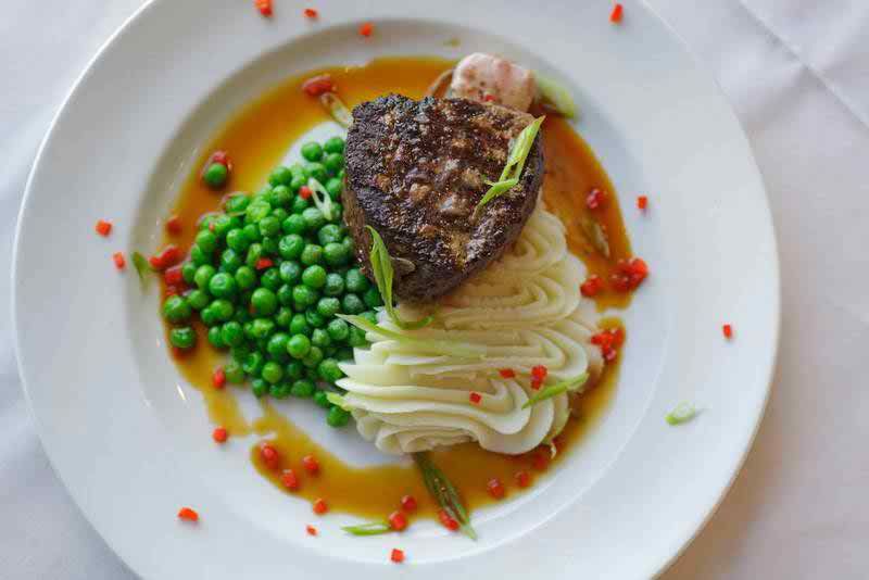 A beautifully plated dish featuring a grilled steak, creamy mashed potatoes, and fresh peas in a savory sauce.