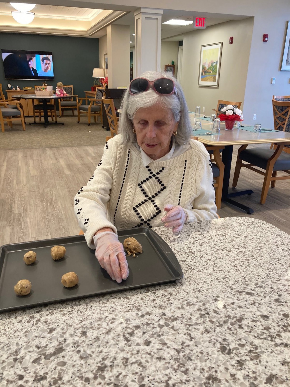 An elderly woman places cookie dough on a baking tray in a kitchen setting.