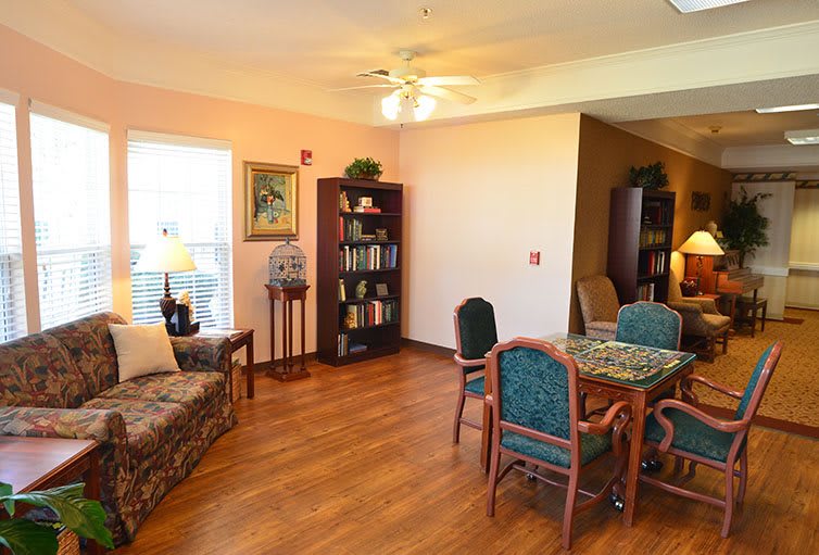 A cozy living and dining area with hardwood floors, featuring a sofa, bookshelf, table, and chairs.