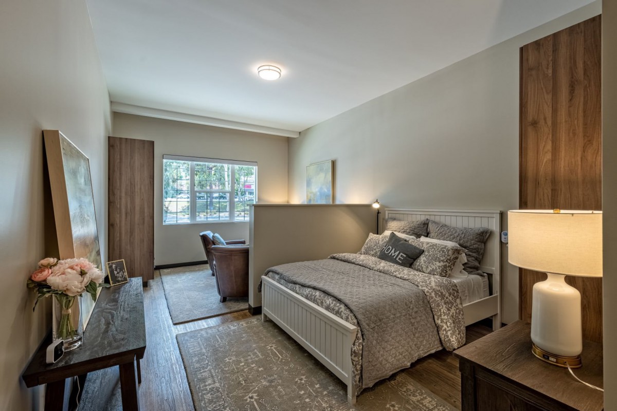 A well-decorated bedroom with a bed, side tables, and a large window allowing natural light.