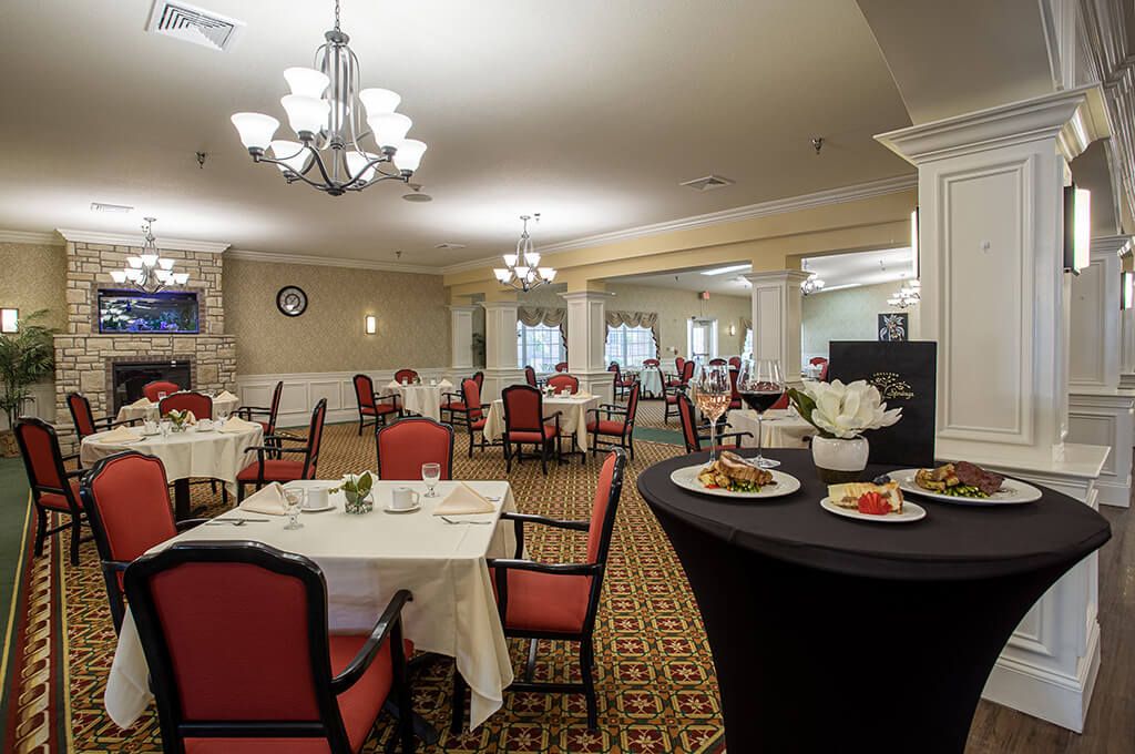 A spacious dining area with elegantly set tables and red chairs, featuring chandeliers and a patterned carpet.