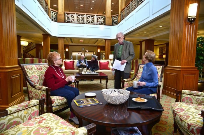 A group of people engaged in conversation in a hotel lobby seating area.