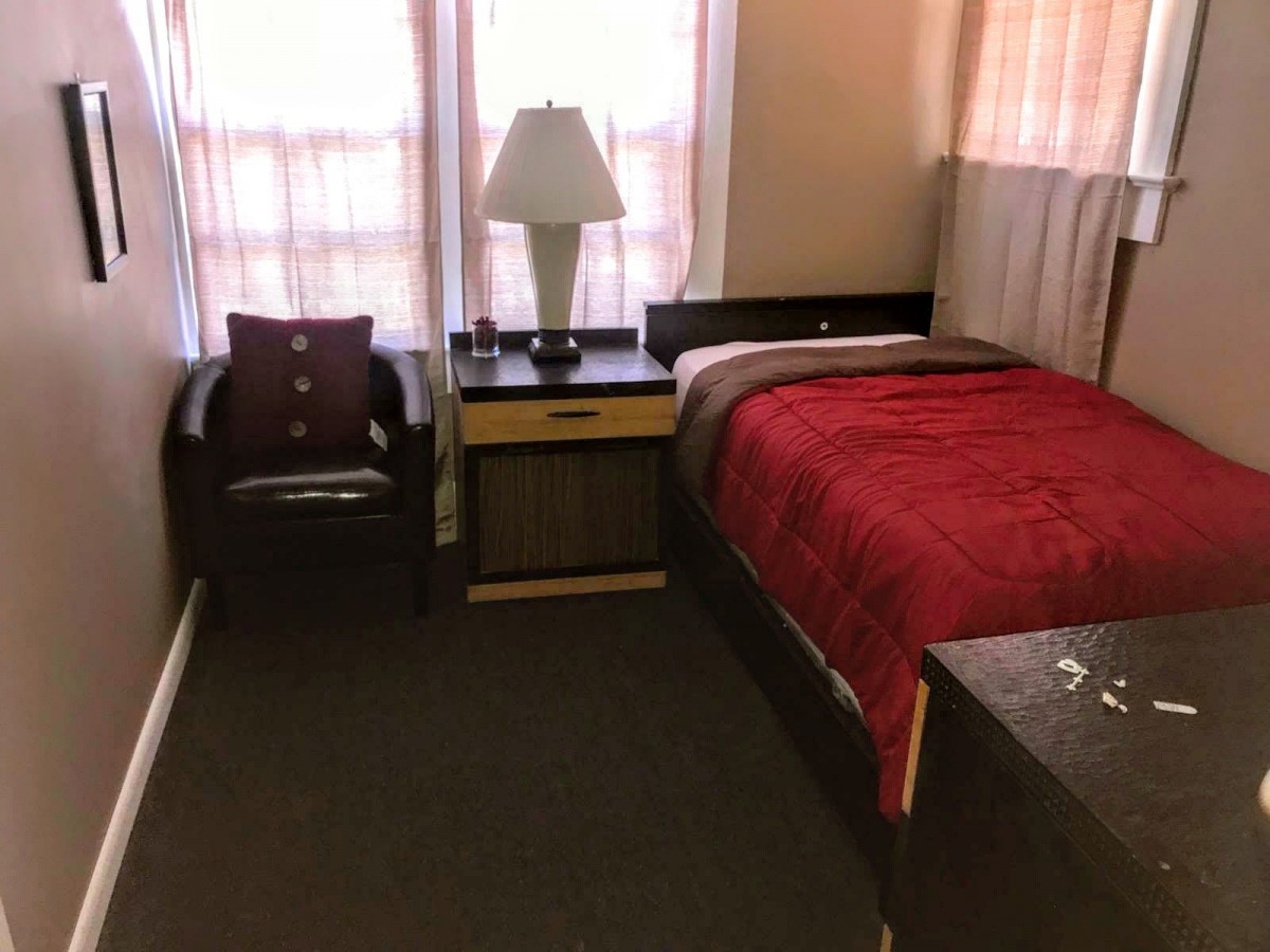 A cozy bedroom setup with a single bed, nightstand, lamp, and chair.