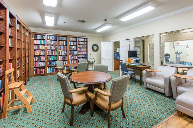 A cozy library interior with bookshelves, a round table, chairs, and a computer workspace.