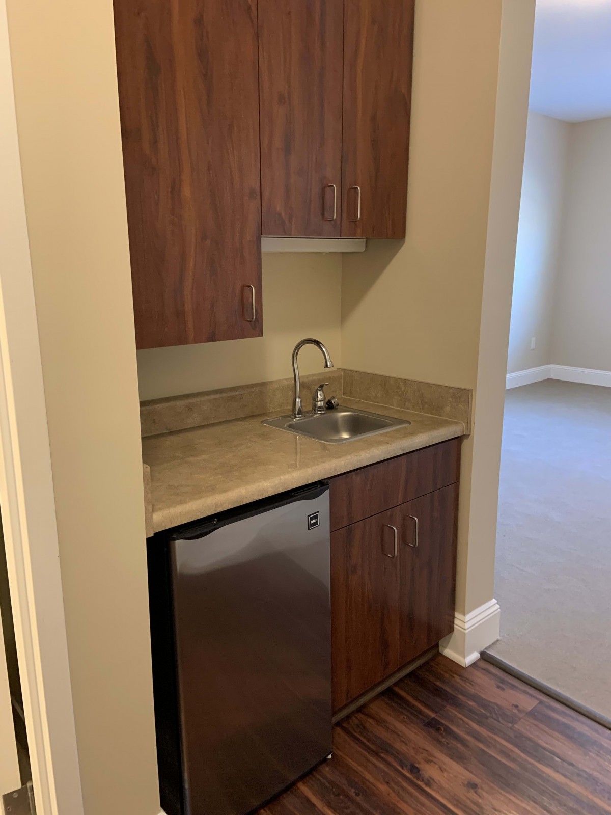A compact kitchenette with wooden cabinets, a sink, and a mini fridge in an apartment.