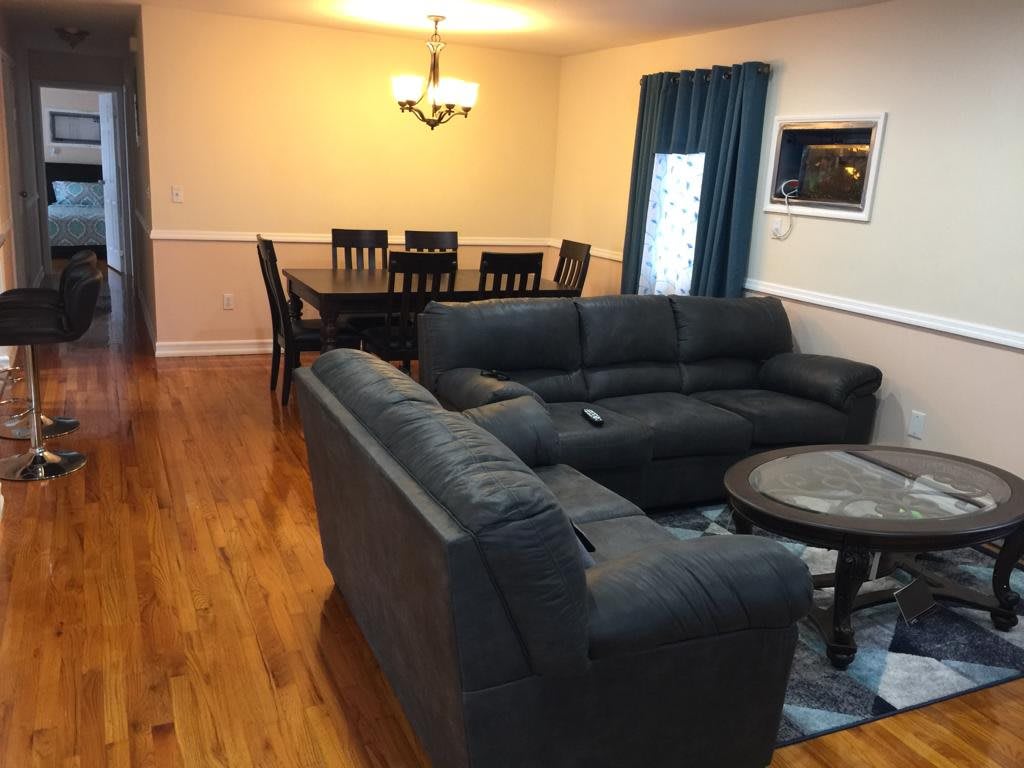 A cozy living room with a connected dining area, featuring comfortable sofas and a wooden dining set.
