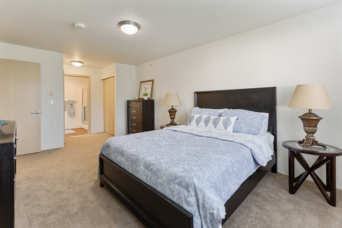 A spacious bedroom with a neatly made bed, dark wooden furniture, and soft carpeting.