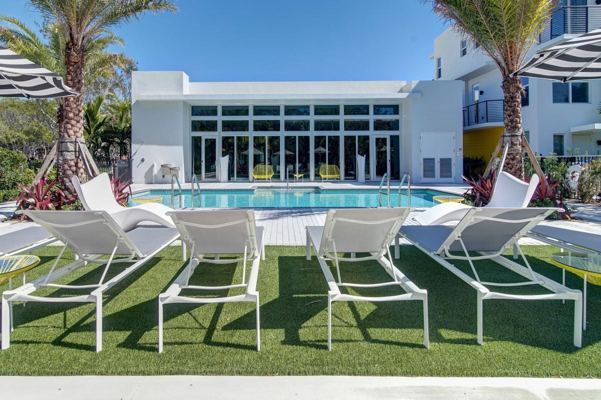 A modern resort featuring a swimming pool with lounge chairs under a clear blue sky.