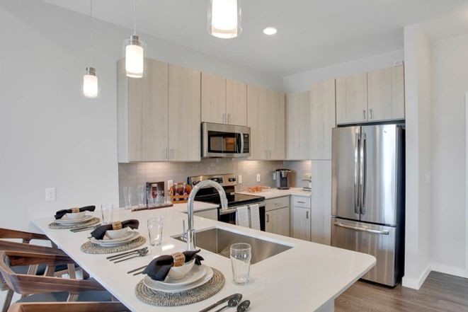 A modern kitchen featuring an island with a sink, stainless steel appliances, pendant lighting, and neatly arranged place settings.