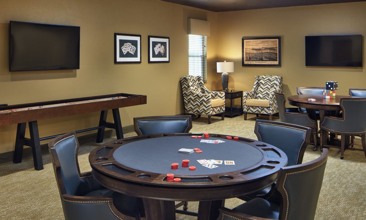 A cozy game room featuring a poker table with cards and chips, surrounded by comfortable chairs and decorated with artwork on the walls.