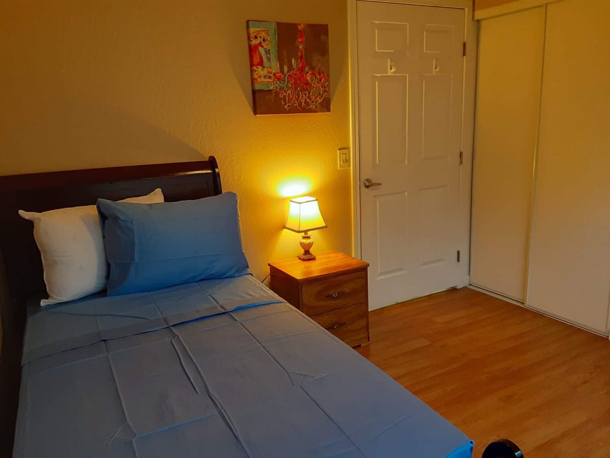 A cozy bedroom with a neatly made bed, nightstand, and soft lamp lighting.